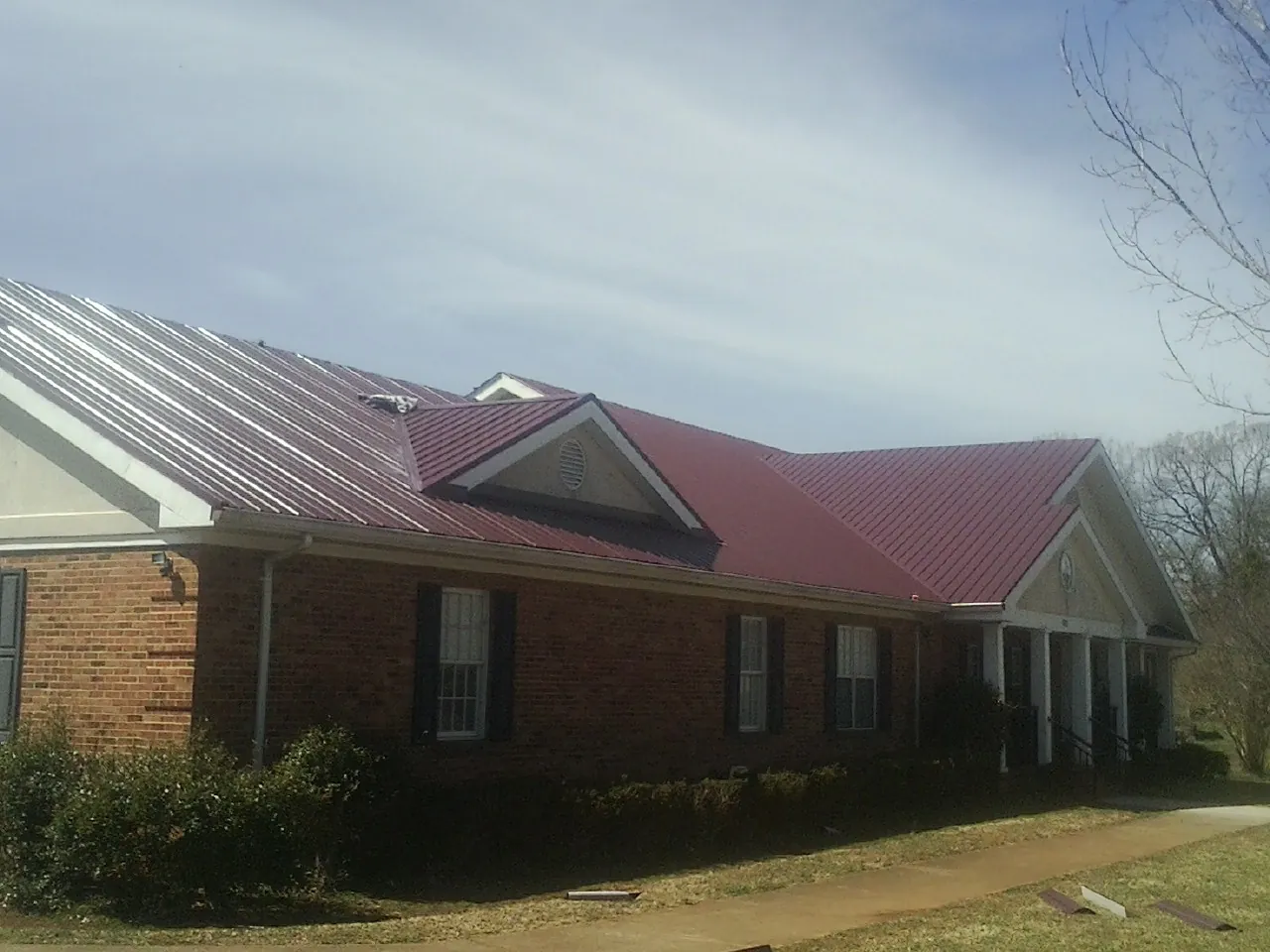 Red metal roof with gabled entries on a long brick building, from a Hail Damage Roof Repair job in Richardsville