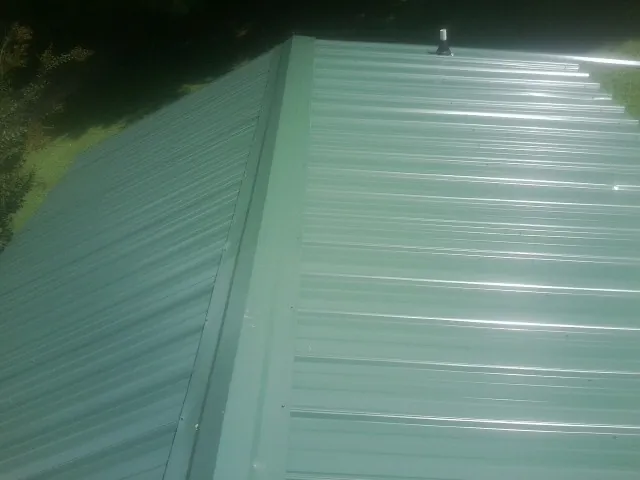 New green metal panels meeting at the ridge of a roof — Flat Roof Repair work by our crew in Richardsville