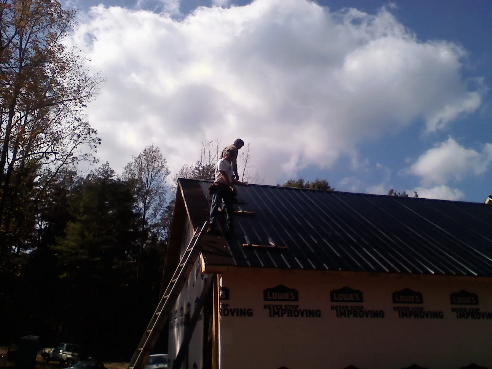 Roofer fastening dark metal panels high against a cloudy sky, from a Roof Inspection job in Richardsville