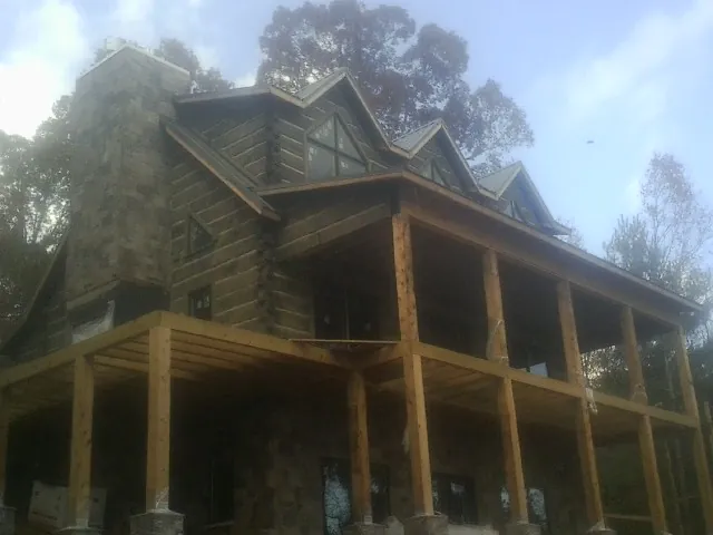 Stone chimney and dormers on a large log home with a timber porch in Richardsville