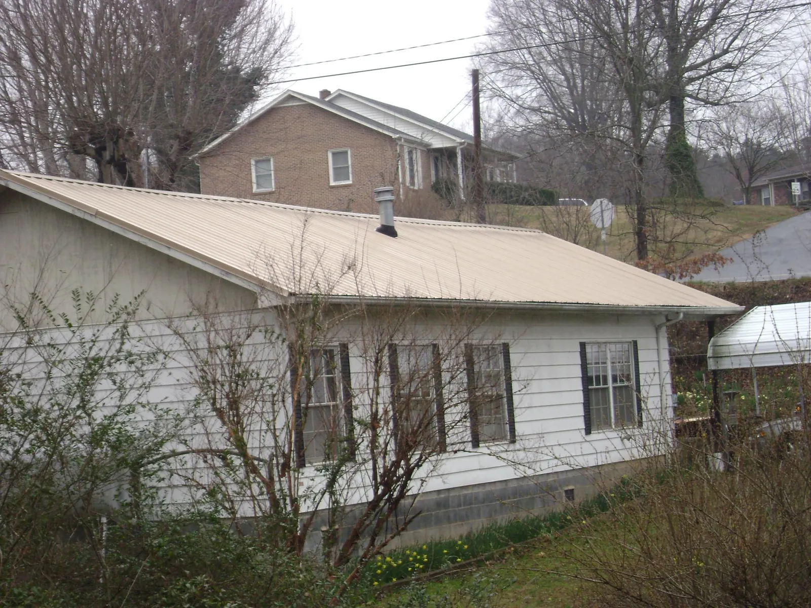 Tan metal roof on a white sided house set into a hillside — Commercial Roofing by Roofing Brothers in Richardsville